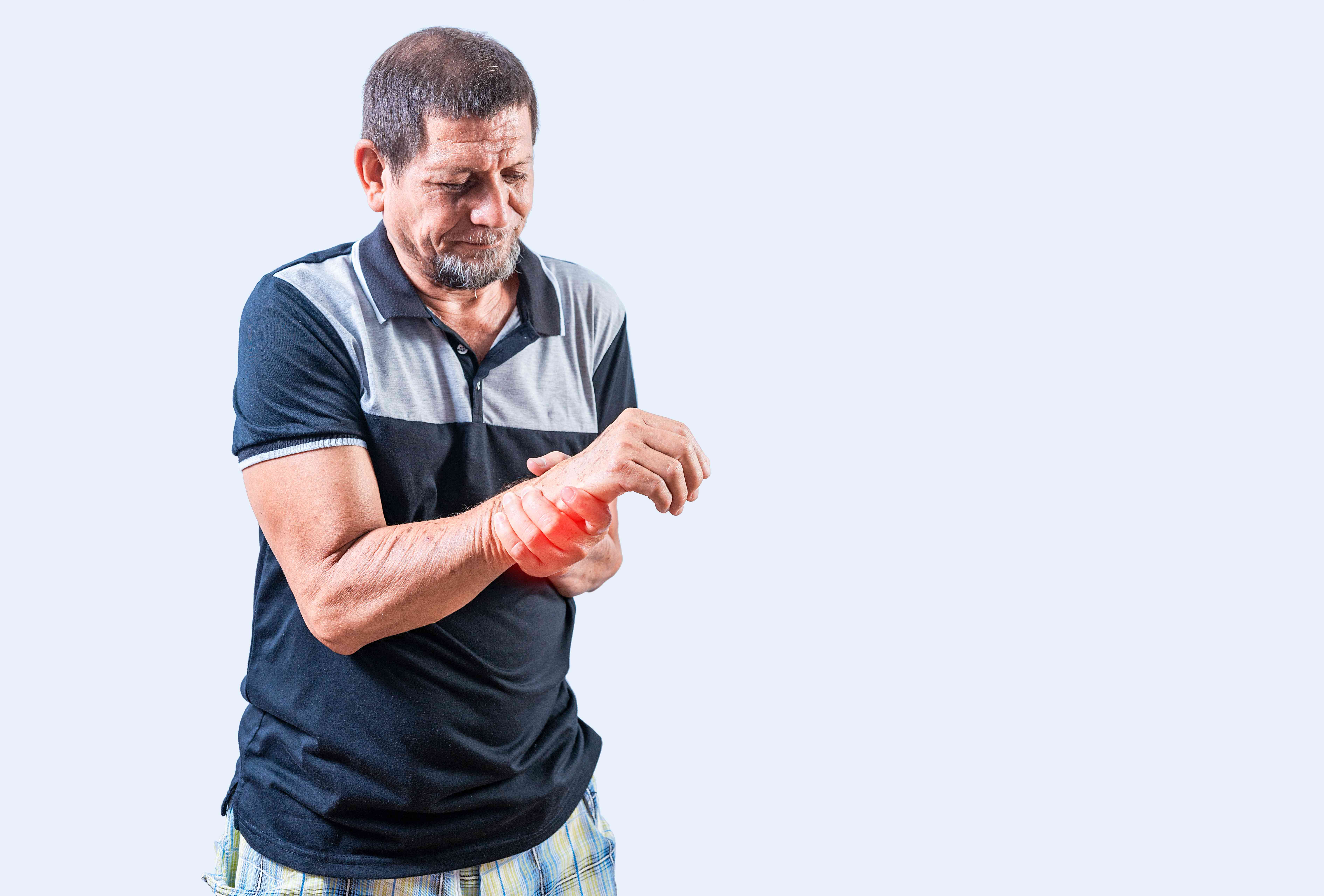  An older man wearing a black and grey shirt holds his wrist with a pained expression, indicating wrist pain or arthritis.